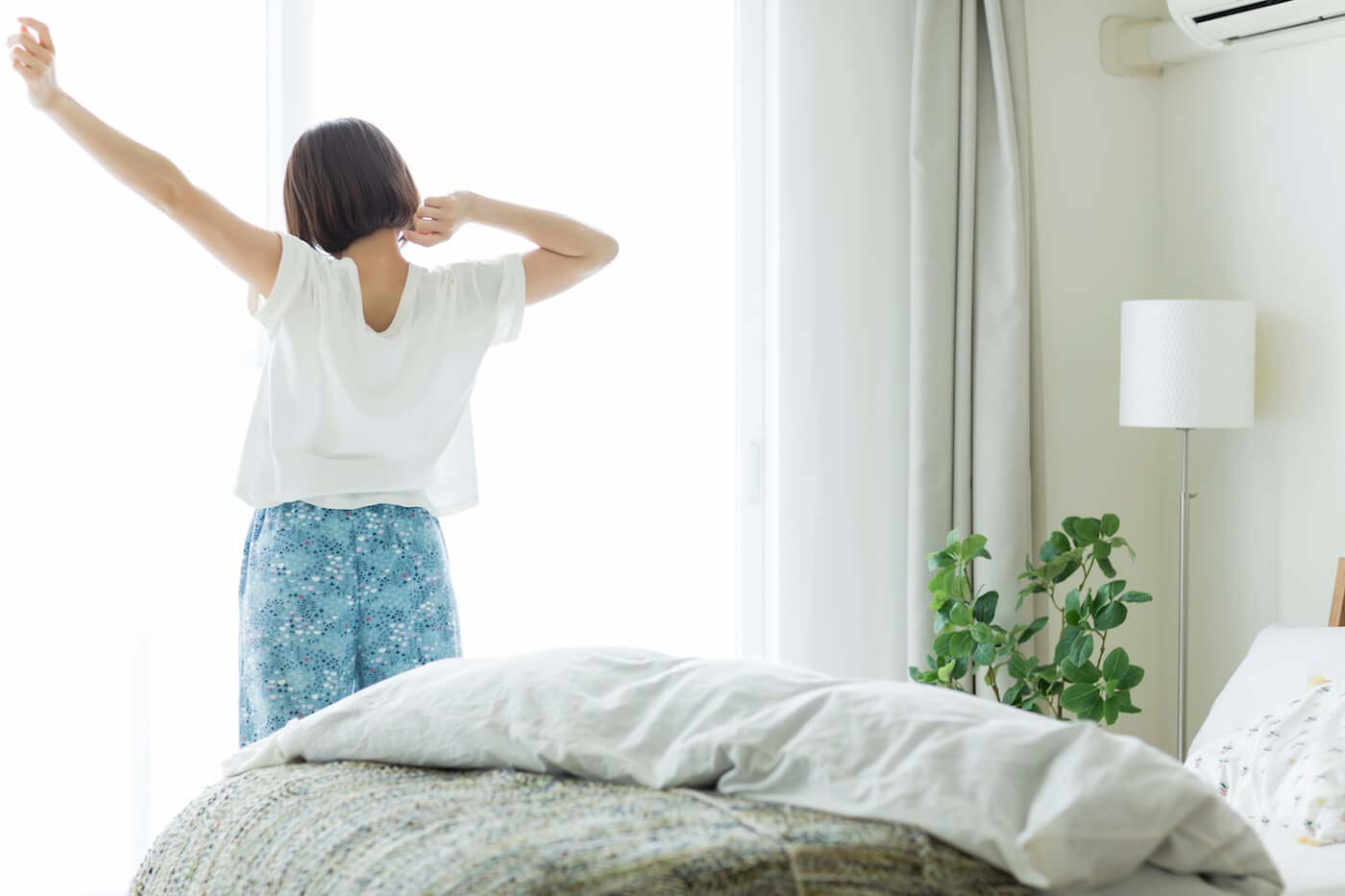 窓際で朝陽を浴びて背伸びする女性
