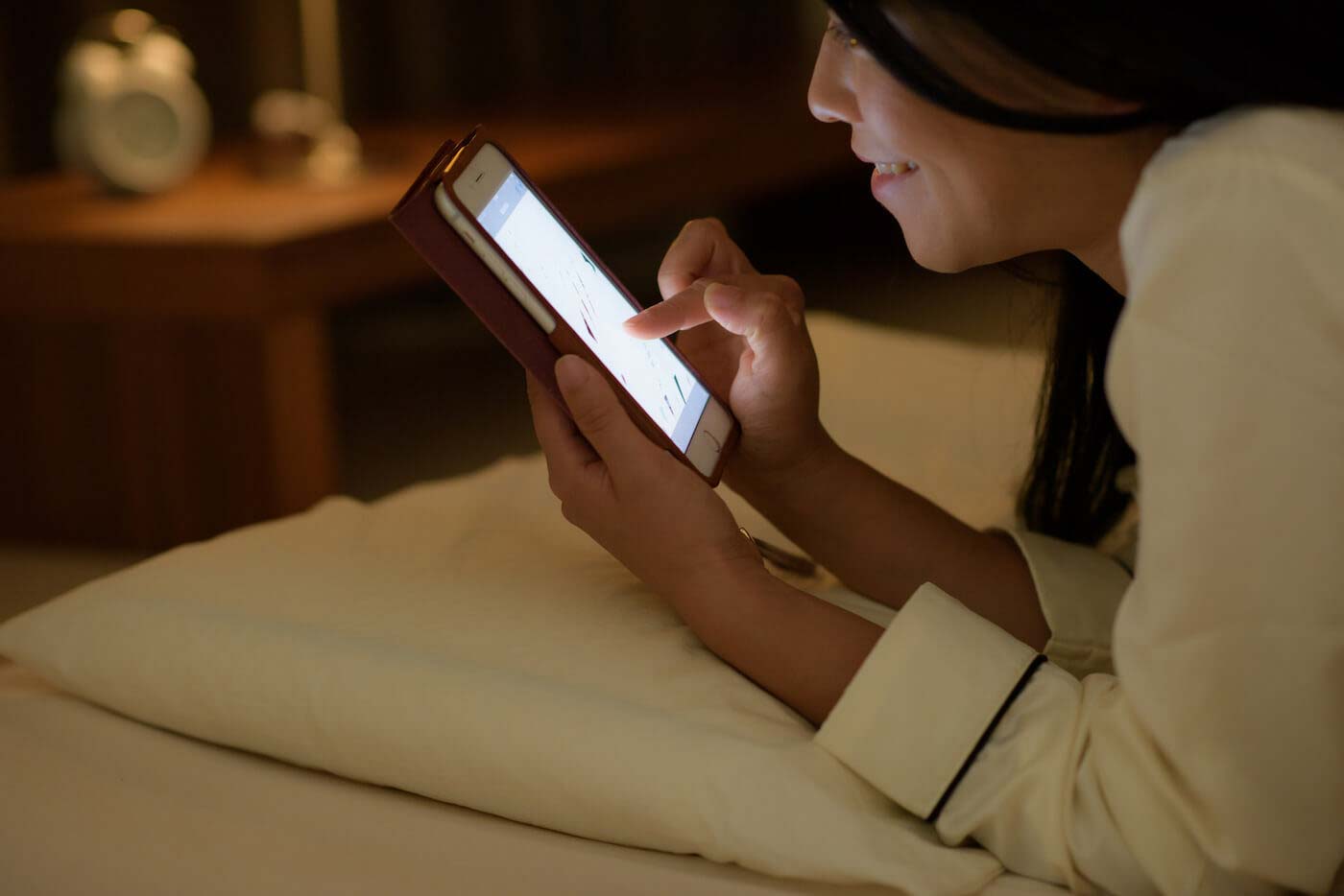 夜にベッドの上でスマホを見ている女性