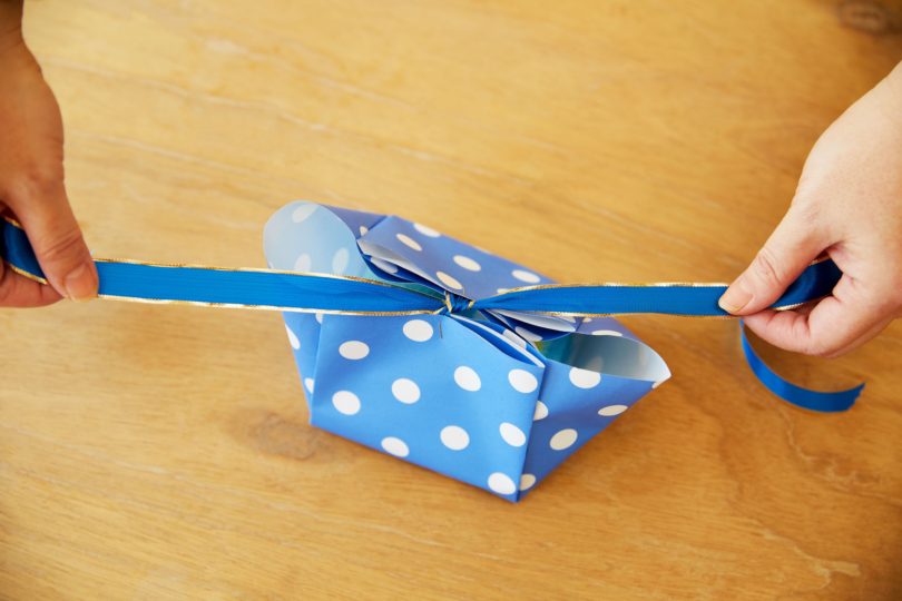 ステップ6の箱にタオルを詰め、留めたリボンを蝶結びし、ホチキスの針を隠すようにシールを貼る。
