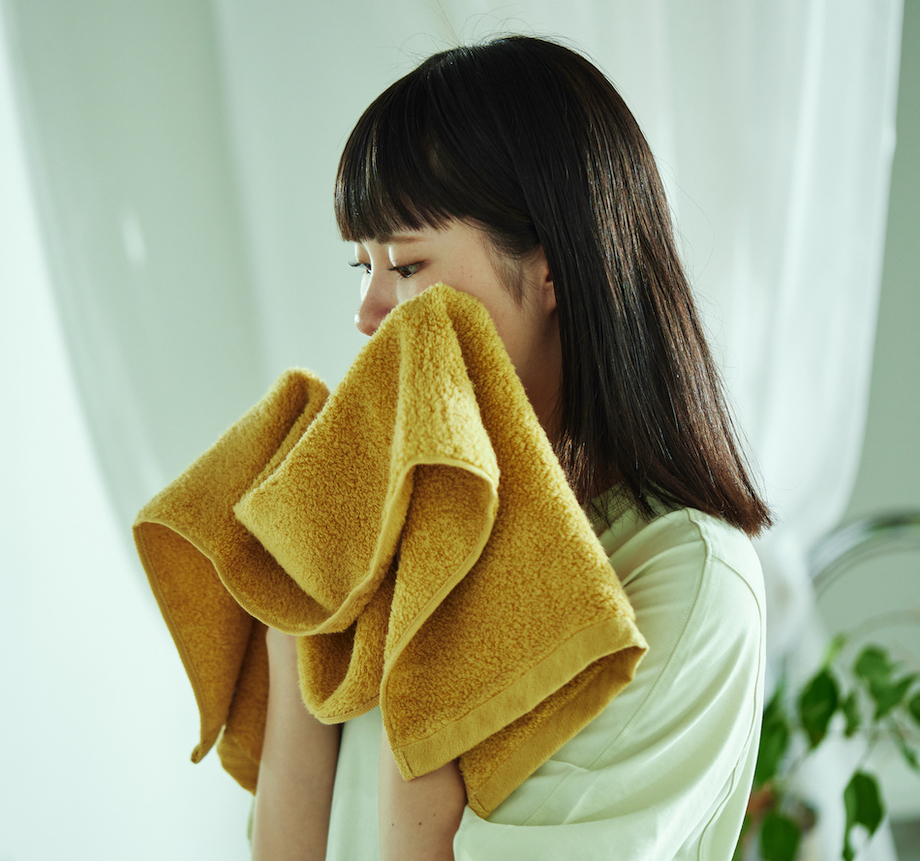 黄朽葉カラーのタオルを顔に当てる女性
